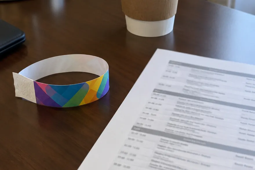 A rainbow convention wristband on a hotel desk beside a coffee cup and a printed class schedule.